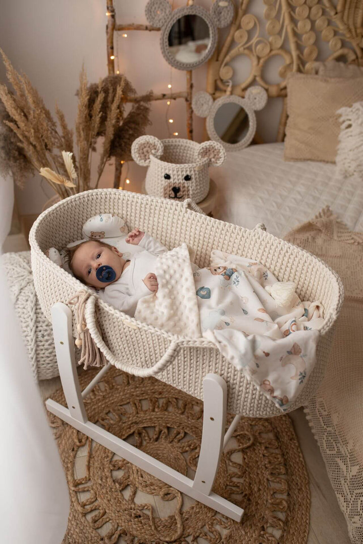 Baby in a cream crochet moses basket with a white wooden stand